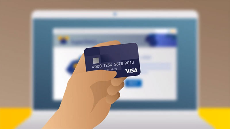 An image of a hand holding a payment card in front of a laptop, used for safe online shopping. 