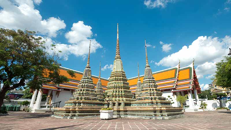 Photograph of five spires grandly decorated in a courtyard by a tree to book your visit with a credit card in Bangkok.