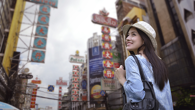 Young asian woman traveler with a backpack on her shoulder and travel hat walking on footpath over China town, Bangkok, Thailand, Travel holiday relaxation concept